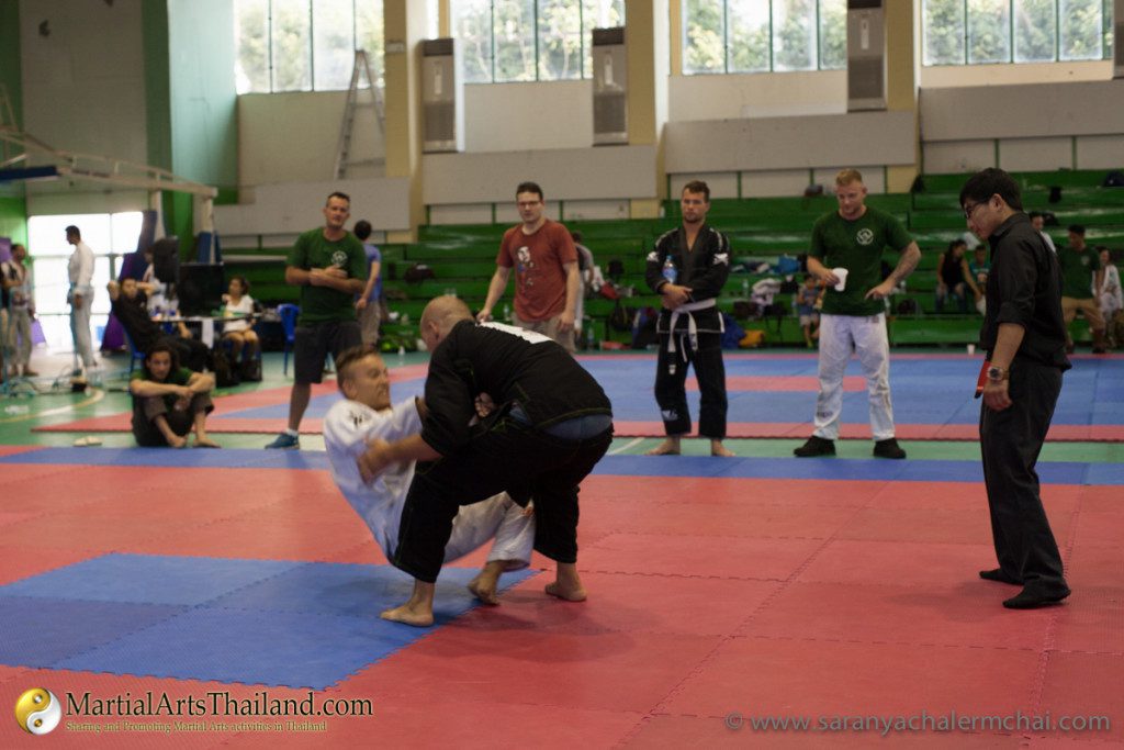 athlete pulling down black gi opponent with people standing in background