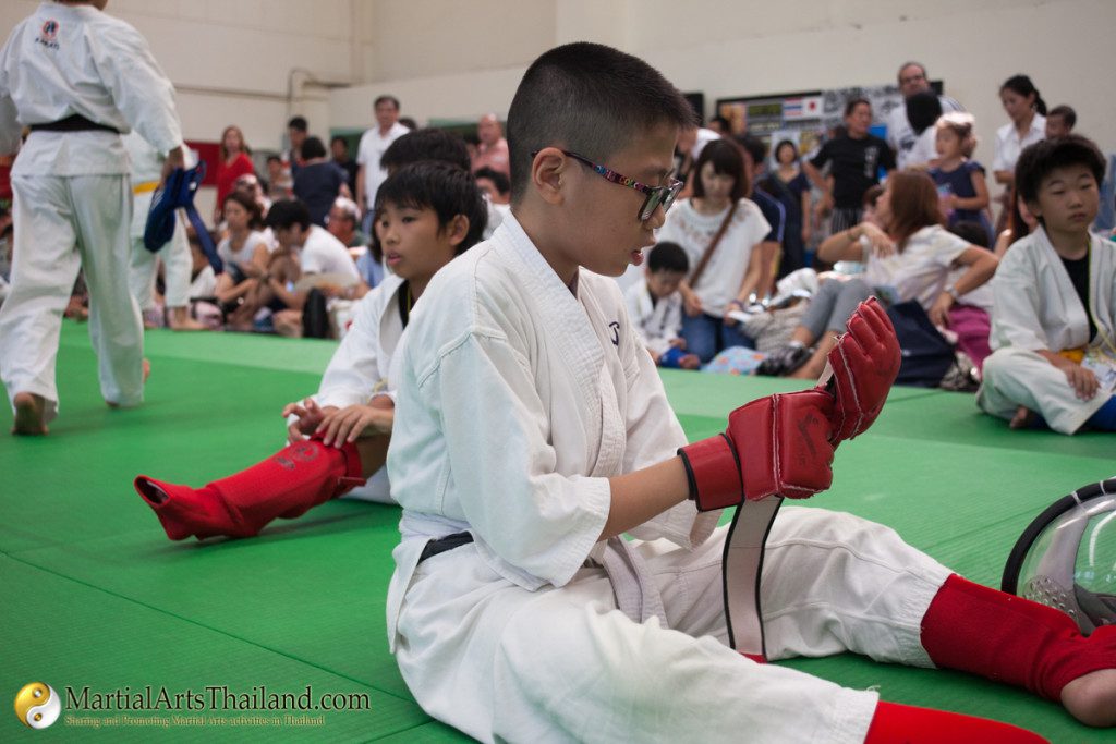 kid wearing glasses adjusting his gloves while sitting on mat