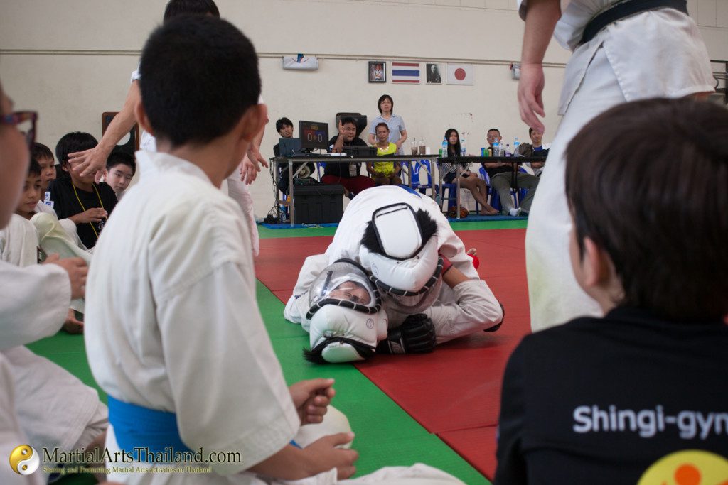 2 fighters on ground bjj while kids watch mat side
