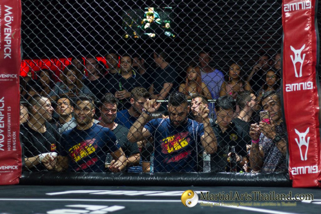 bangkok fight lab coaches watching the fight thru the mma cage net at Full Metal Dojo 13 Concrete Jungle