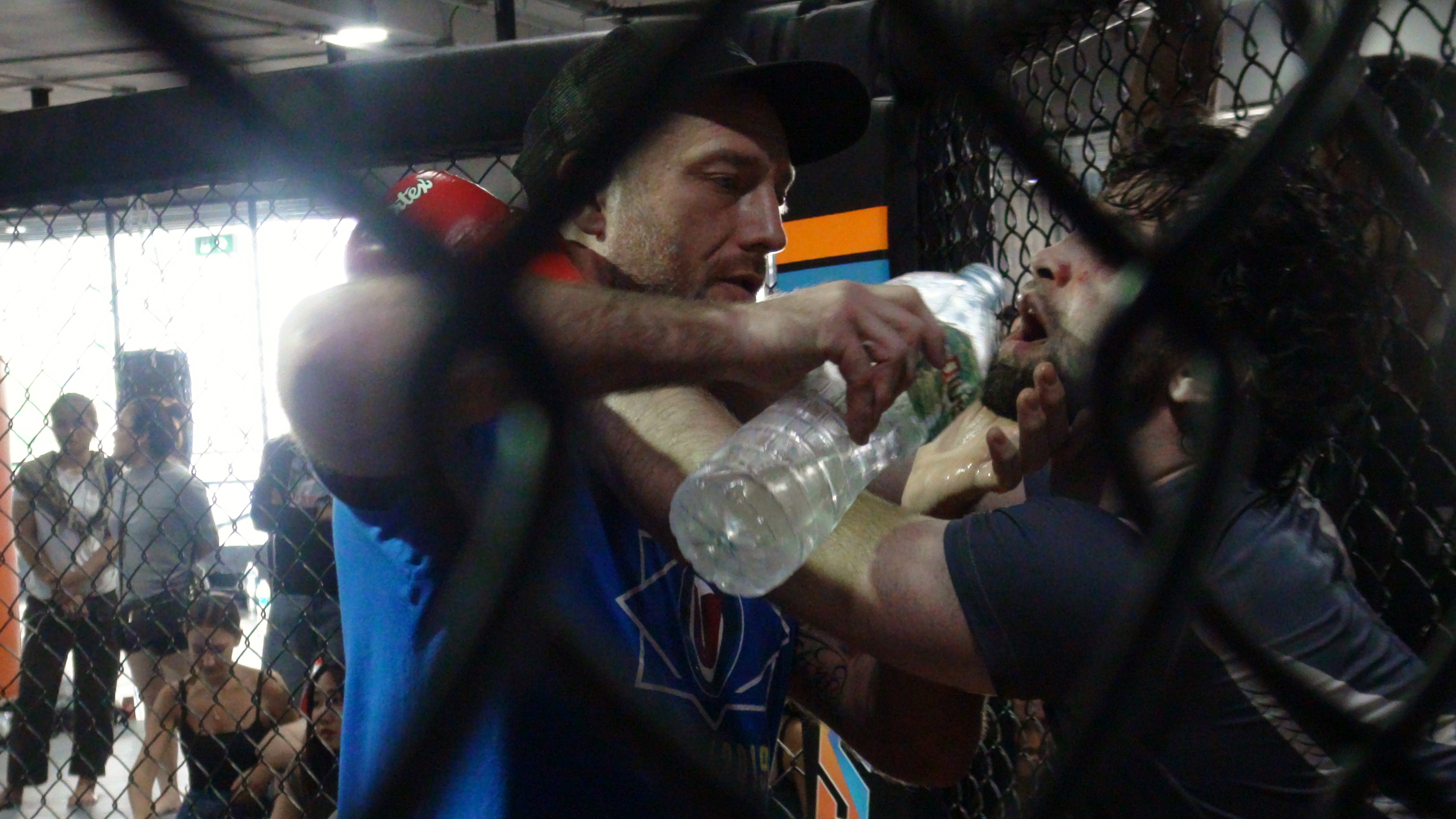 Coach giving water to a MMA cage fighter between rounds