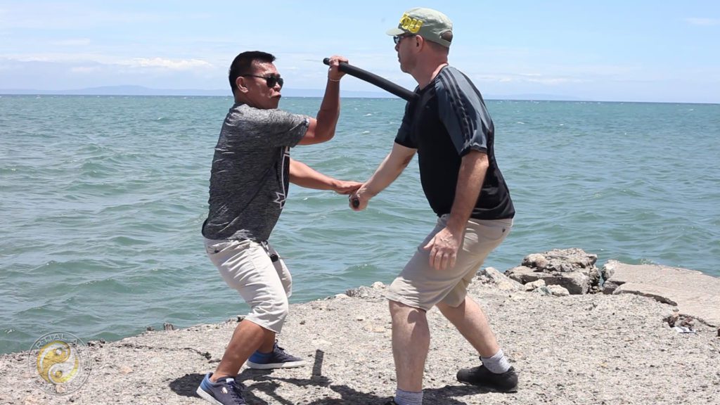 Jun Carin and Lwigh Harris demonstrating Eskrima on a rock at the sea shore