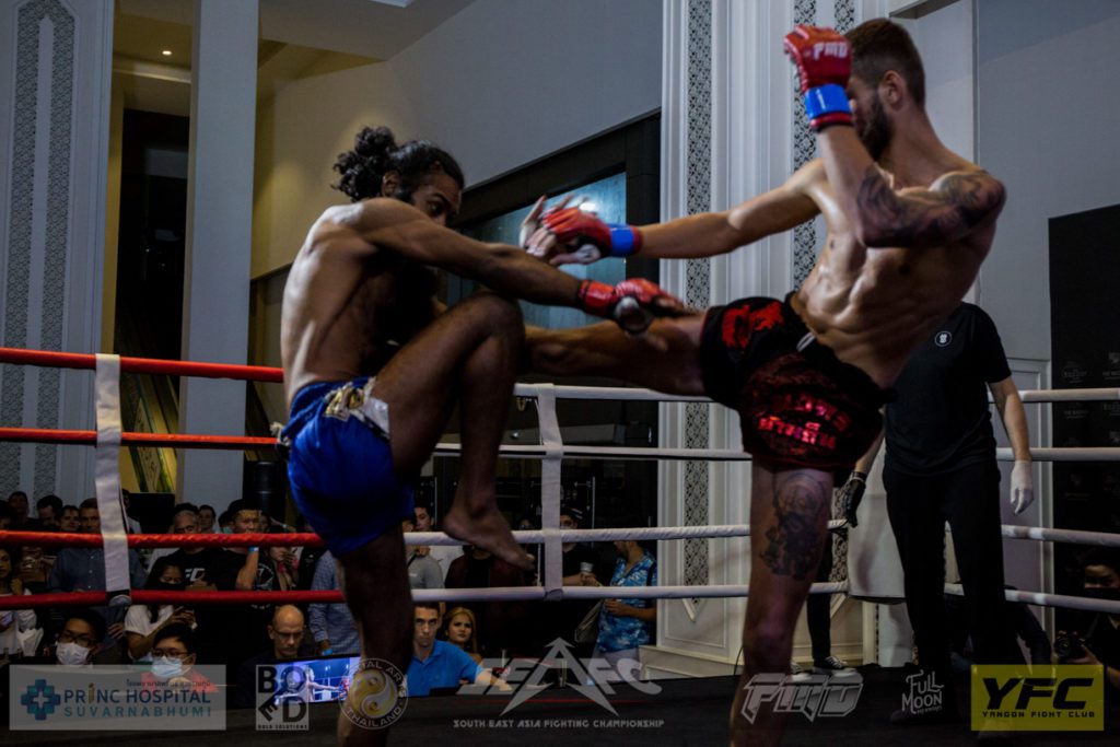 Charles Mainier throwing a roundhouse kick to Alex Parmit Singh who blocks with his shin during their Full Metal Muay Thai fight