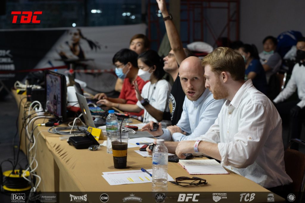 Commentators Ali McOnie and Jimmy Bowe at the desk with Martial Arts Thailand team in the background